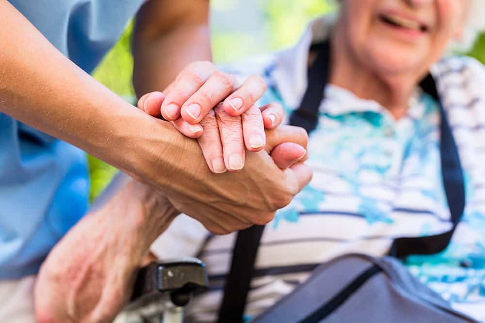 A caregiver at an assisted living facility holding the hand of a senior resident