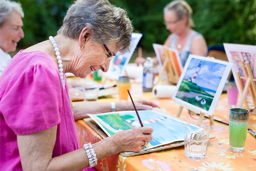 A senior outside on a sunny day painting a picture of a lighthouse